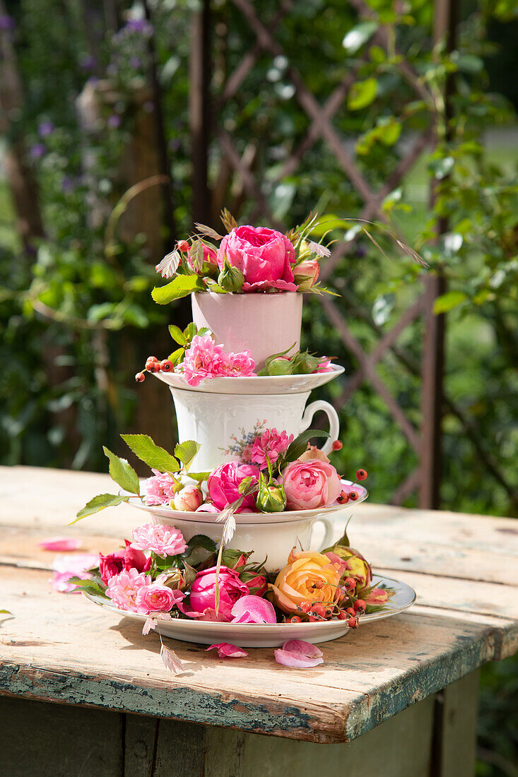 Stacked teacups with rose decoration on a rustic wooden table in the garden