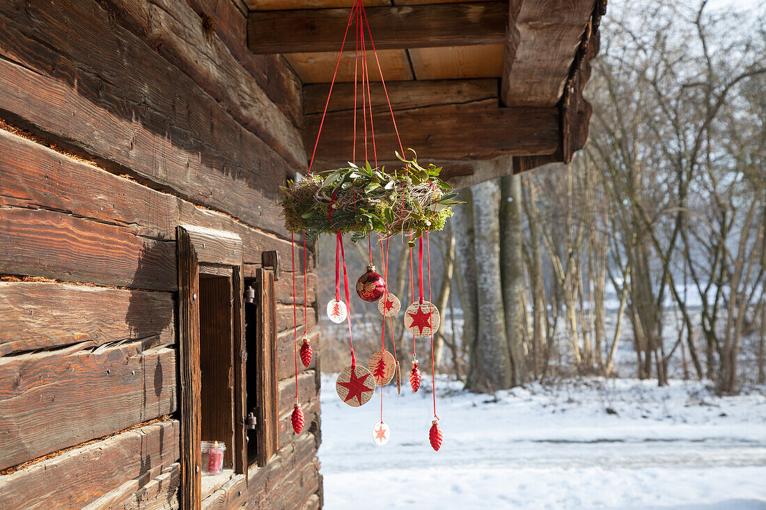 Weihnachtlicher Kranz mit roten Anhängern an rustikaler Holzhütte