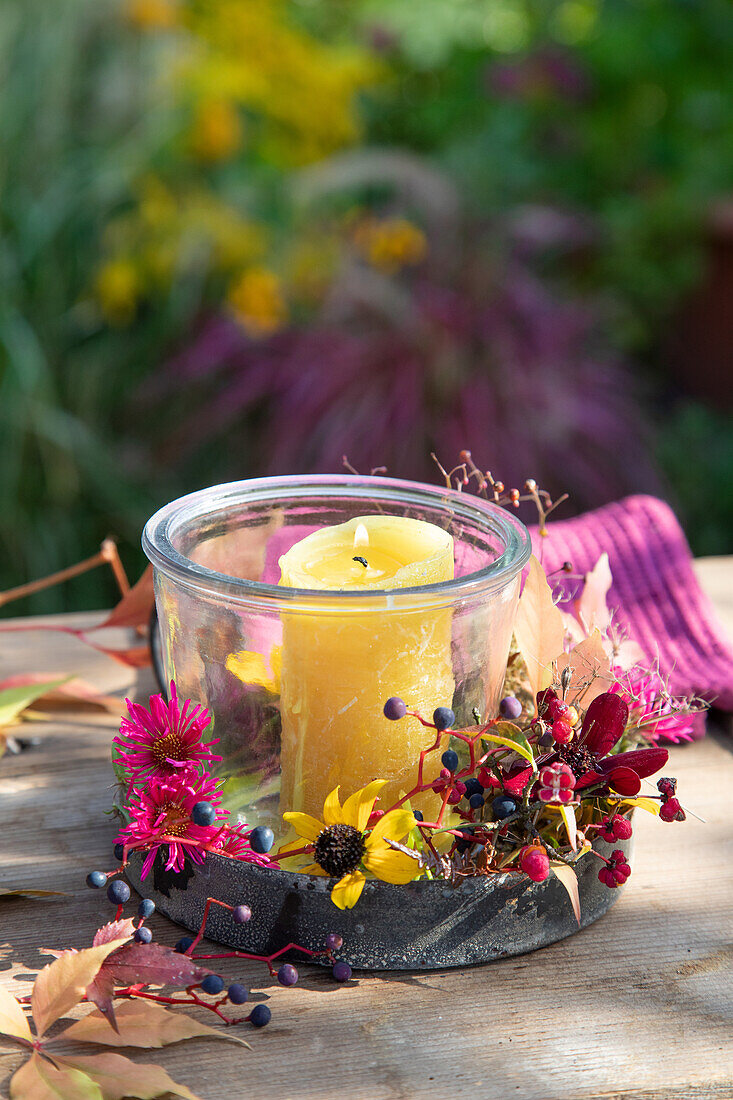 Bunter Herbstkranz mit Windlicht und bunten Blüten auf Holztisch im Garten