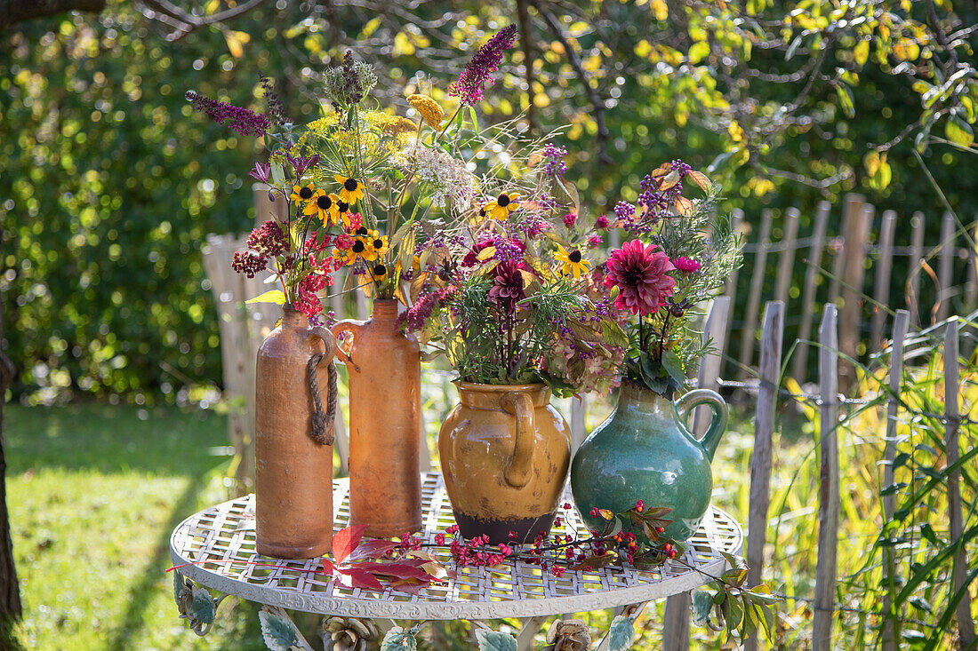 Herbstblumen in rustikalen Vasen auf Metalltisch im Garten