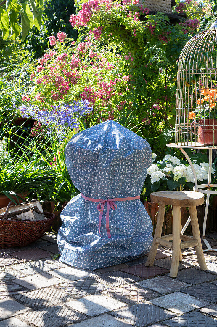 Barbecue with blue and white cover in the flowering garden area