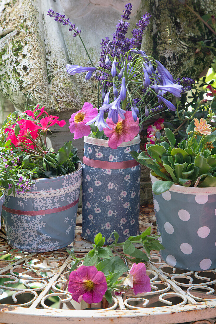 Flowering plant pots with lavender, petunias and geraniums wrapped in decorative fabrics