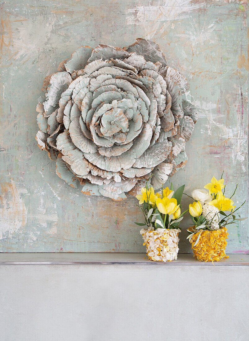 Wall decoration in the shape of a flower and two yellow and white flower arrangements in colorfully decorated pots