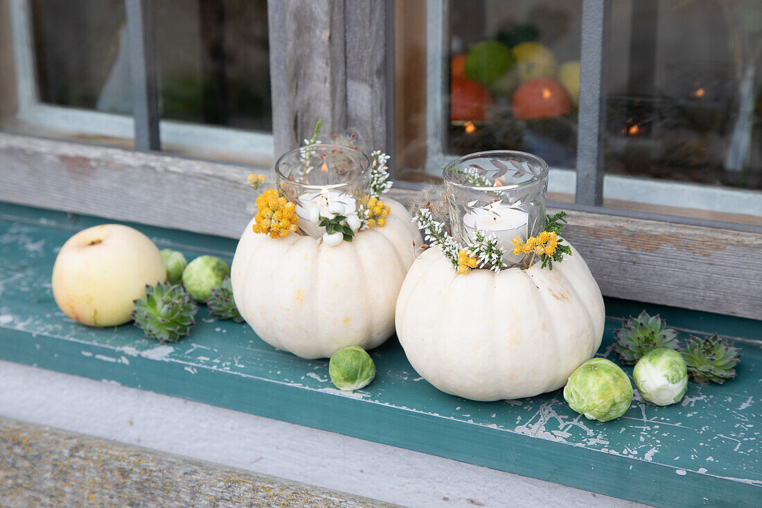 White pumpkins as candle holders with yellow and white flowers on a windowsill