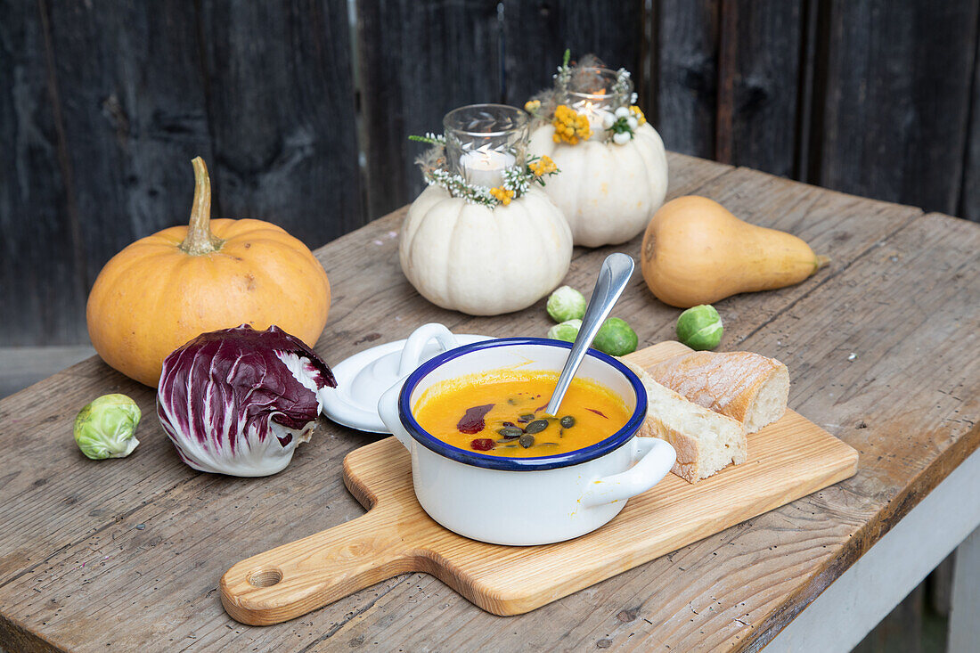 Herbstlich dekorierter Holztisch mit Kürbissuppe, Brot und Radicchio