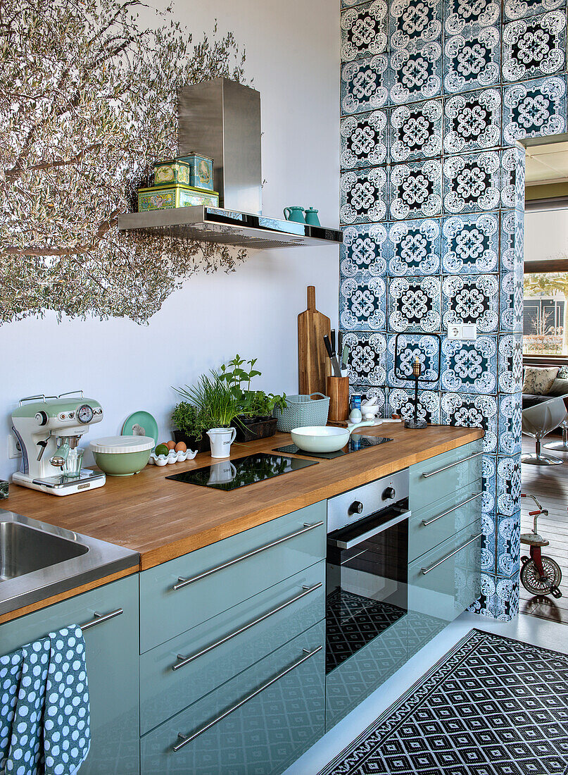 Kitchen with pastel green cabinets, wooden worktop and tile pattern on the wall