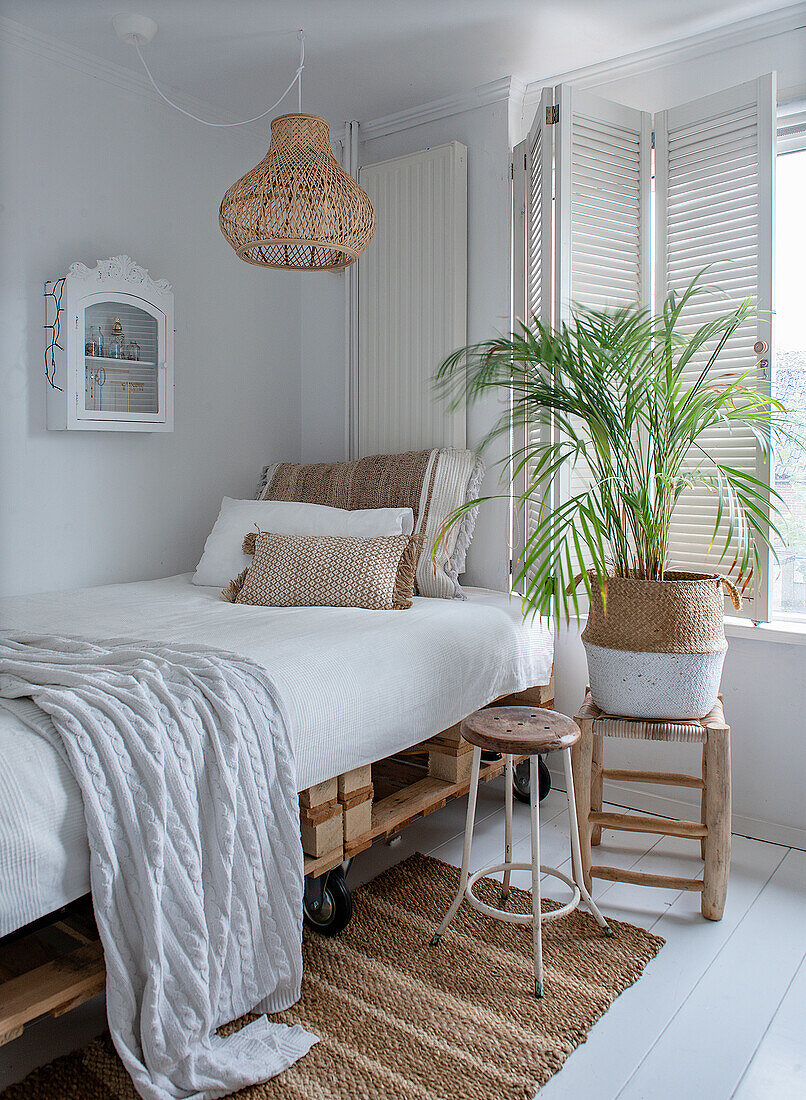 Bright bedroom with bed made from pallets, rattan lamp and green plant