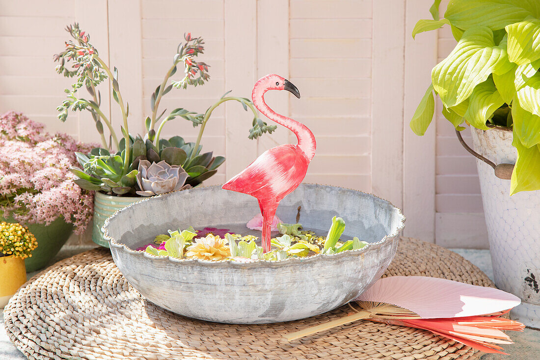 Miniteich mit Blüten und Flamingo-Dekoration auf einer Terrasse