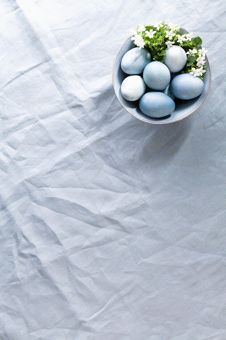 Bowl with blue coloured Easter eggs on linen fabric