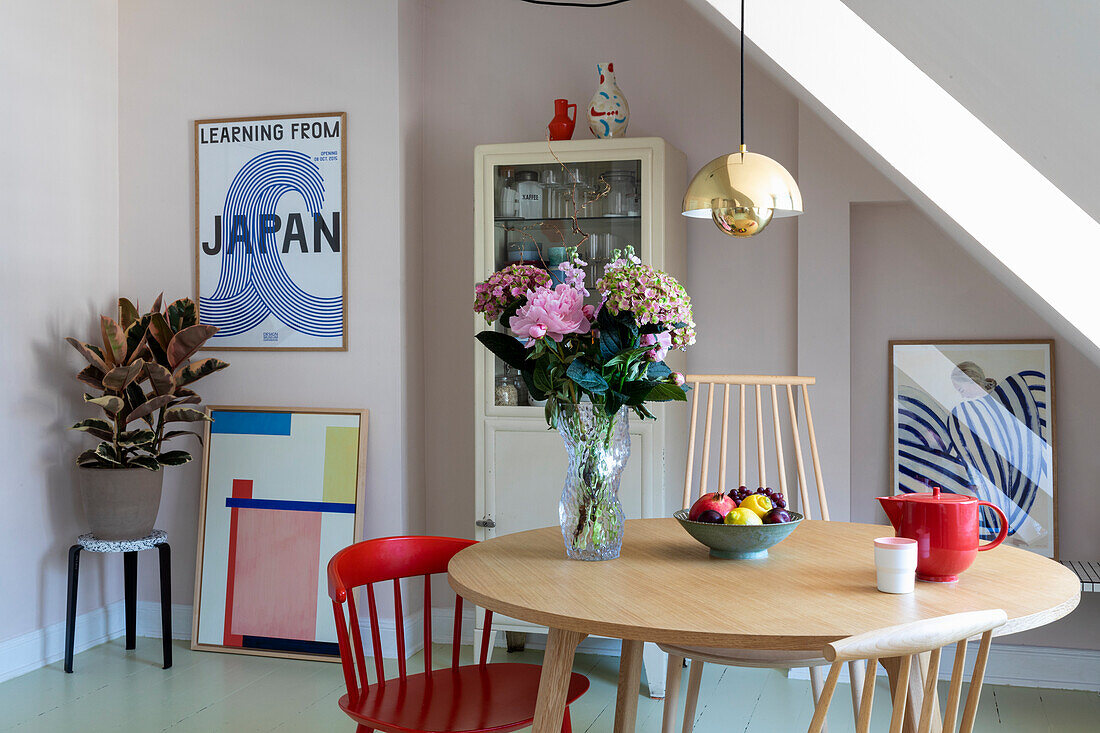 Dining room with round wooden table, golden pendant lamp and modern artwork