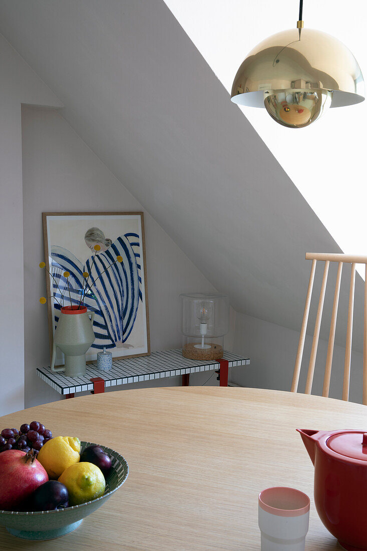 Dining area with round wooden table, fruit bowl and golden hanging lamp