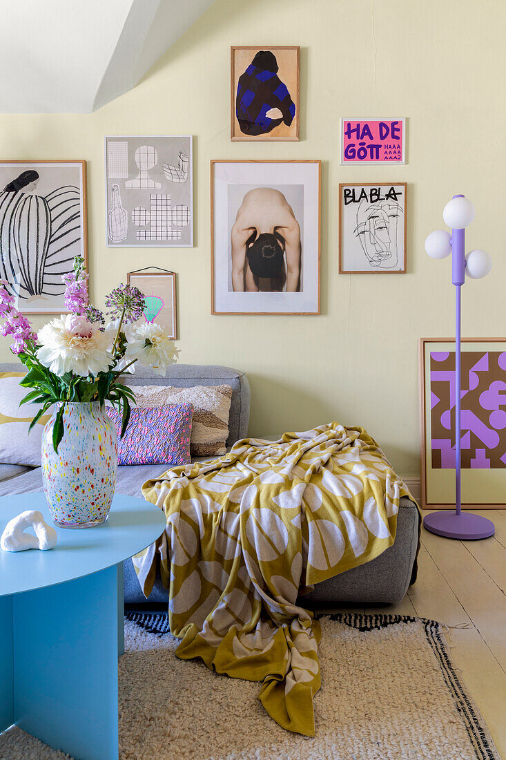 Living room with colourful art gallery and patterned plaid on grey armchair