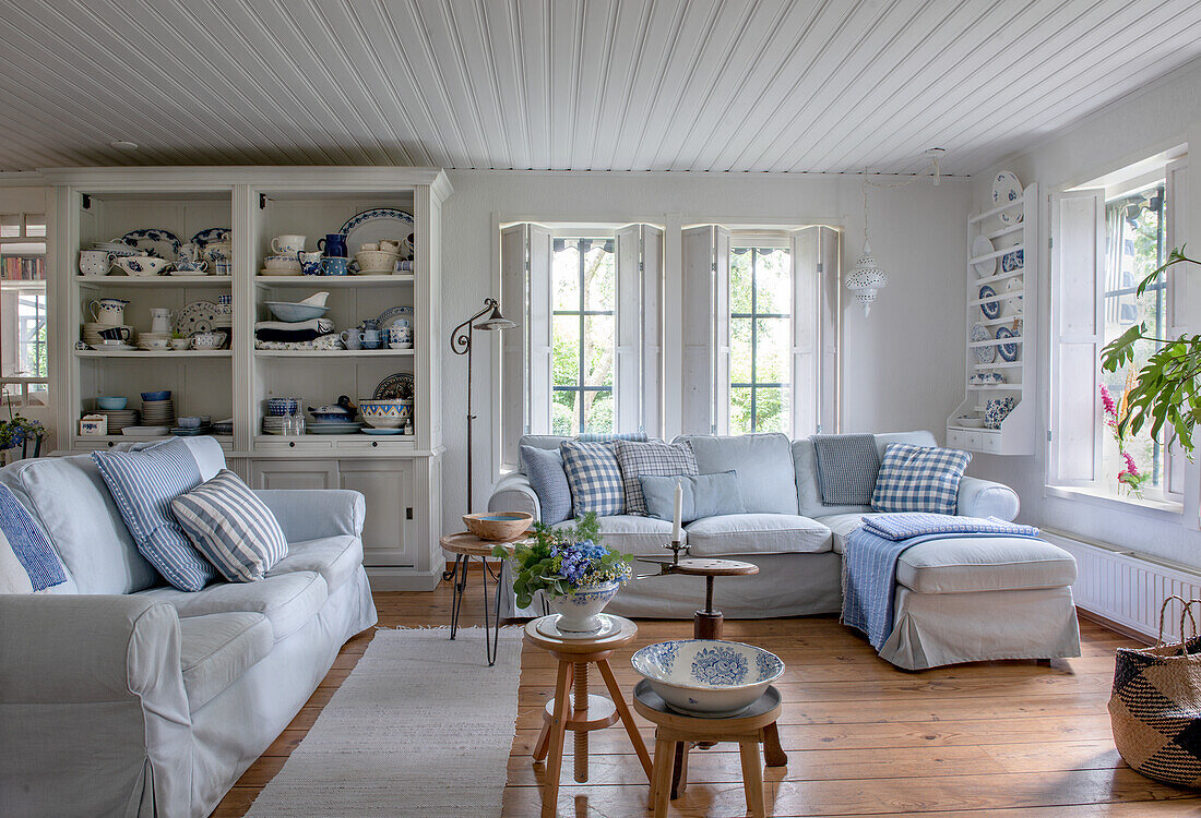 Country-style living room with light-coloured sofas and blue and white cushions, wooden floor and open cupboard