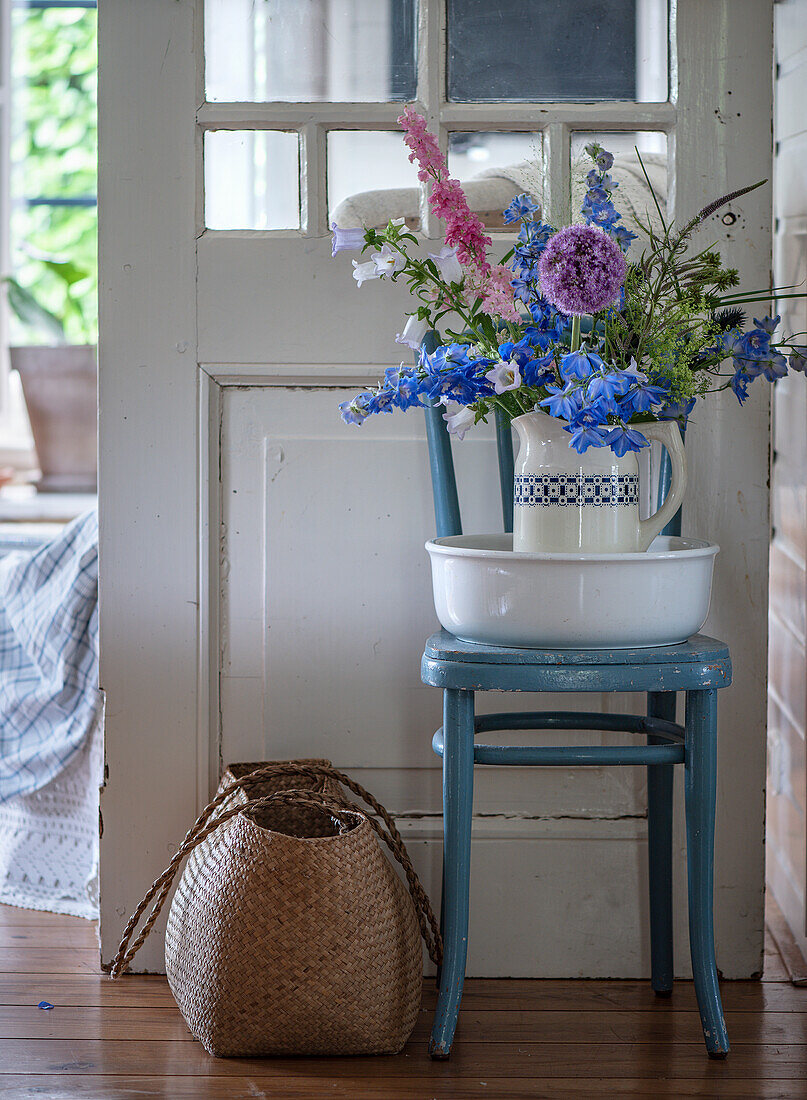 Wiesenblumen im Krug, Waschschüssel und blauer Holzstuhl im Landhausstil