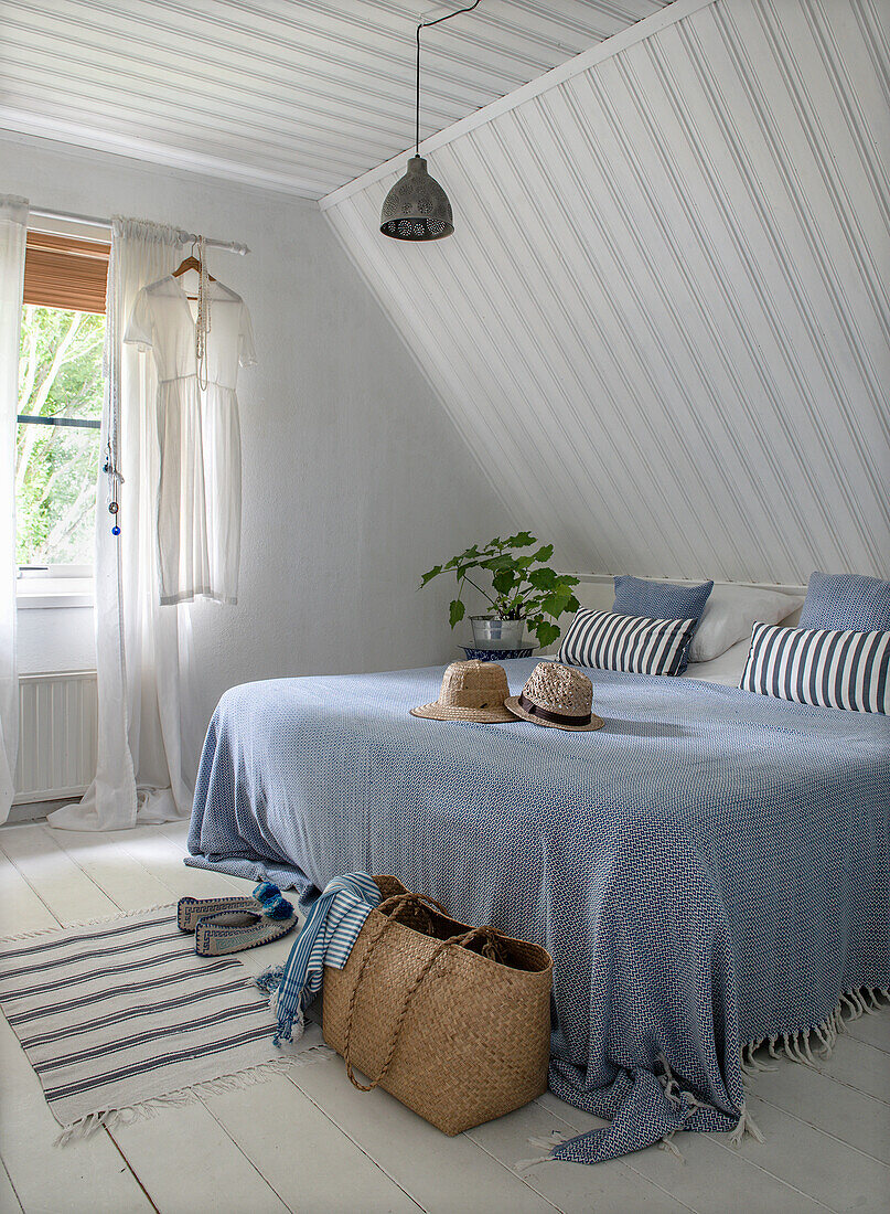 Lichtdurchflutetes Schlafzimmer mit Dachschräge und Doppelbett mit blauer Tagesdecke