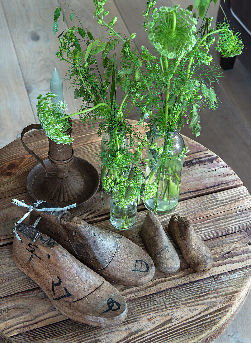 Old wooden shoe lasts and green meadow flowers in glass vases on a round wooden table