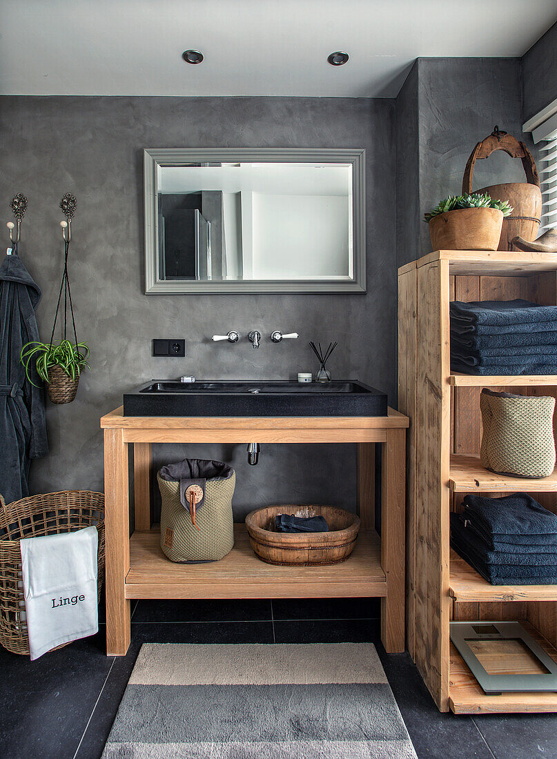 Bathroom with wooden washbasin, grey concrete-look walls and shelf with towels