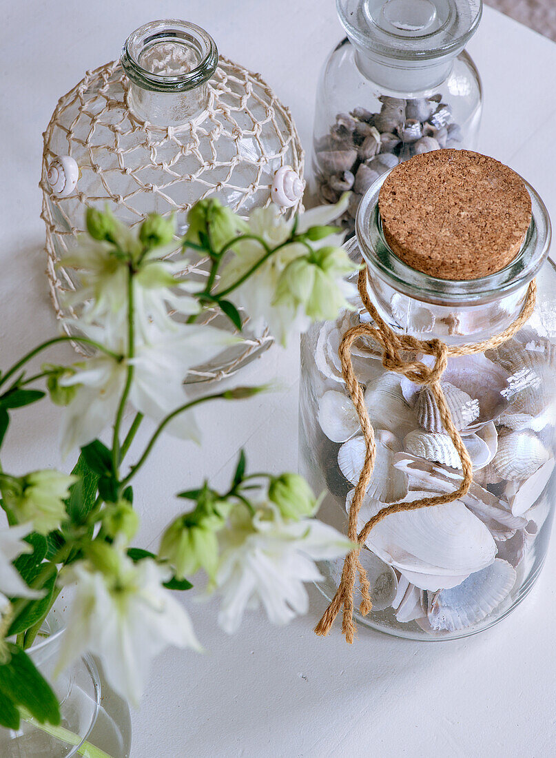 Glasflaschen mit Muscheln und Netz auf weißem Tisch