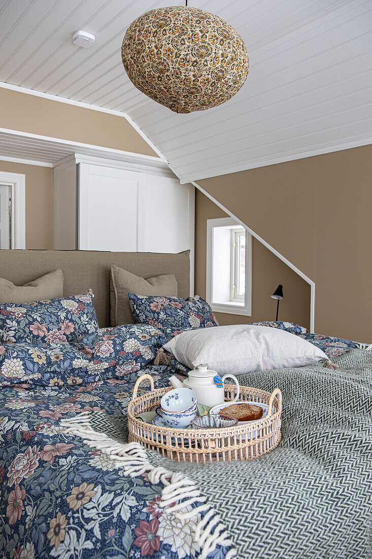 Bedroom with sloping ceiling, floral bed linen and rattan tray on the bed