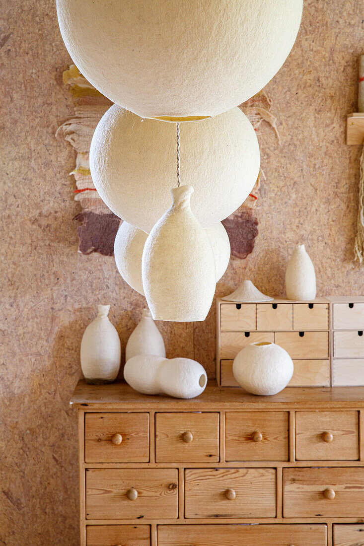 Wooden chest of drawers with white ceramic vases and felt lamps in a rustic room