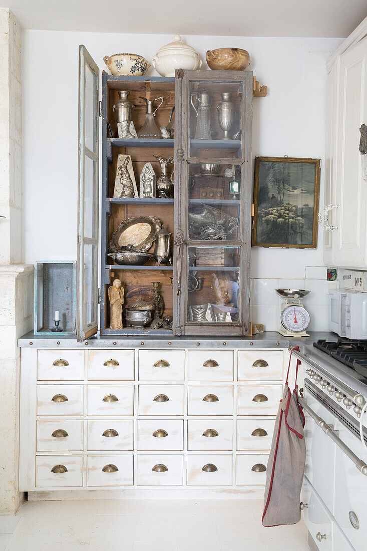 Display cabinet with white drawer unit filled with antique crockery and kitchen utensils