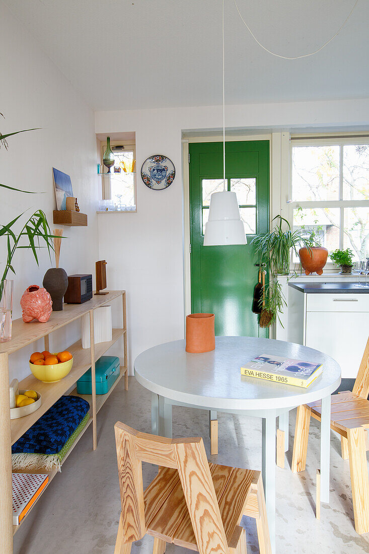 Round dining table with wooden chairs in a light-coloured kitchen with green door