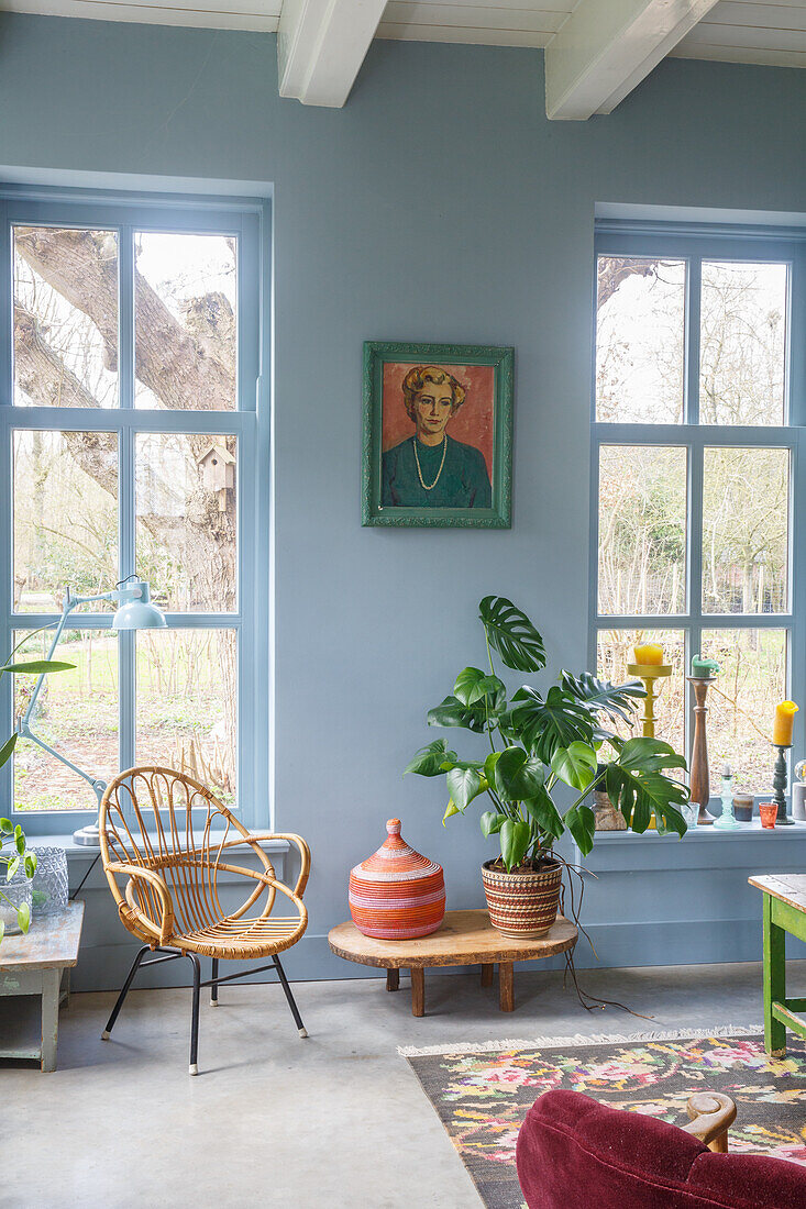 Living room with rattan armchair and monstera plant in front of large windows