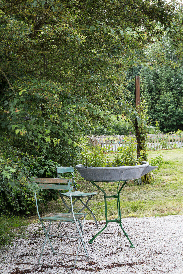 Metallische Gartenmöbel mit bepflanzter Vogeltränke auf Kiesuntergrund