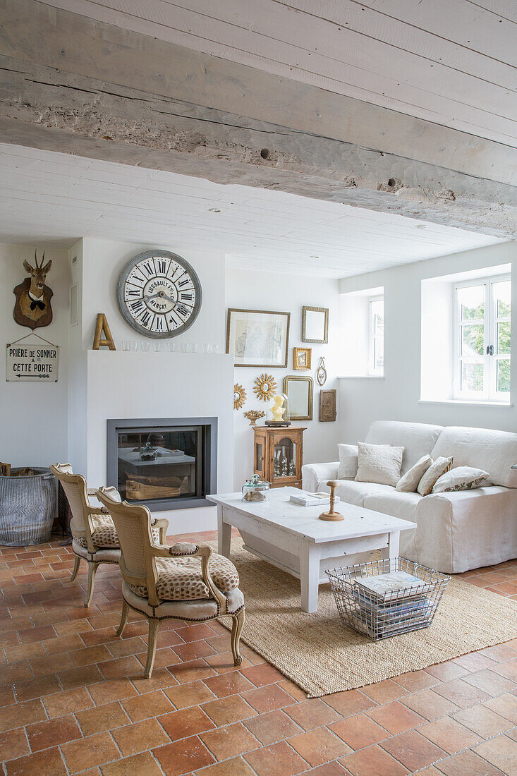 Wohnzimmer im rustikalen Landhausstil mit Terrakottafliesen, weißem Sofa und Kamin