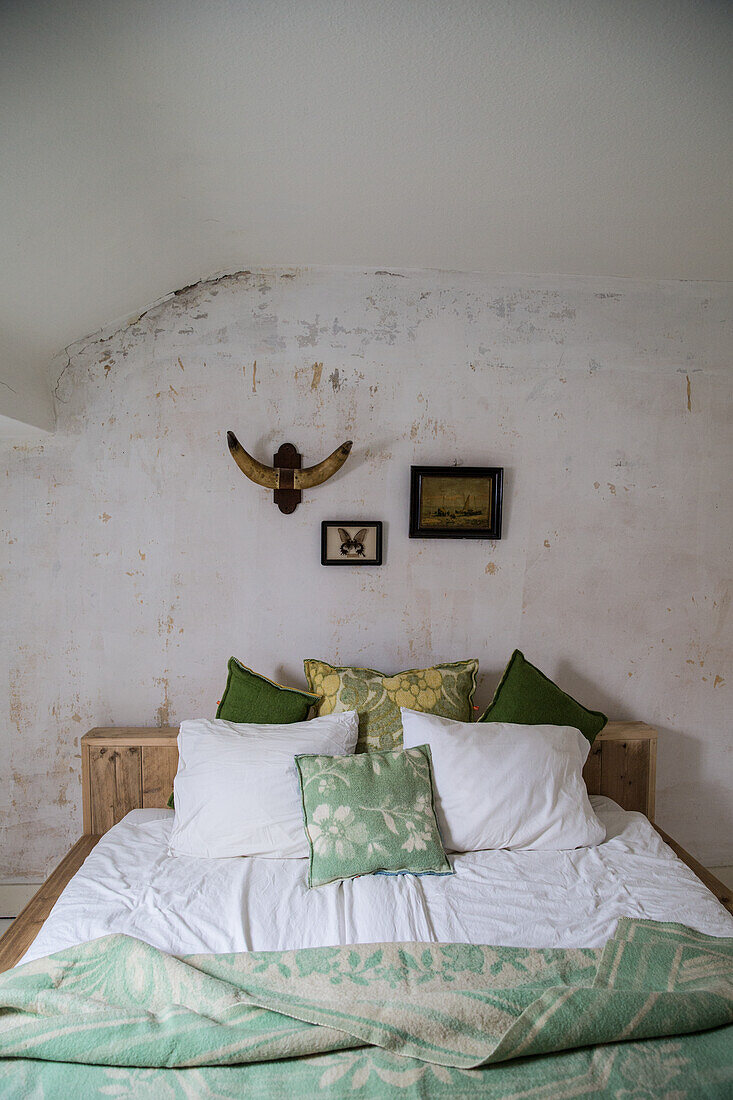 Wooden bed with green and white cushions in front of a rustic wall in the bedroom