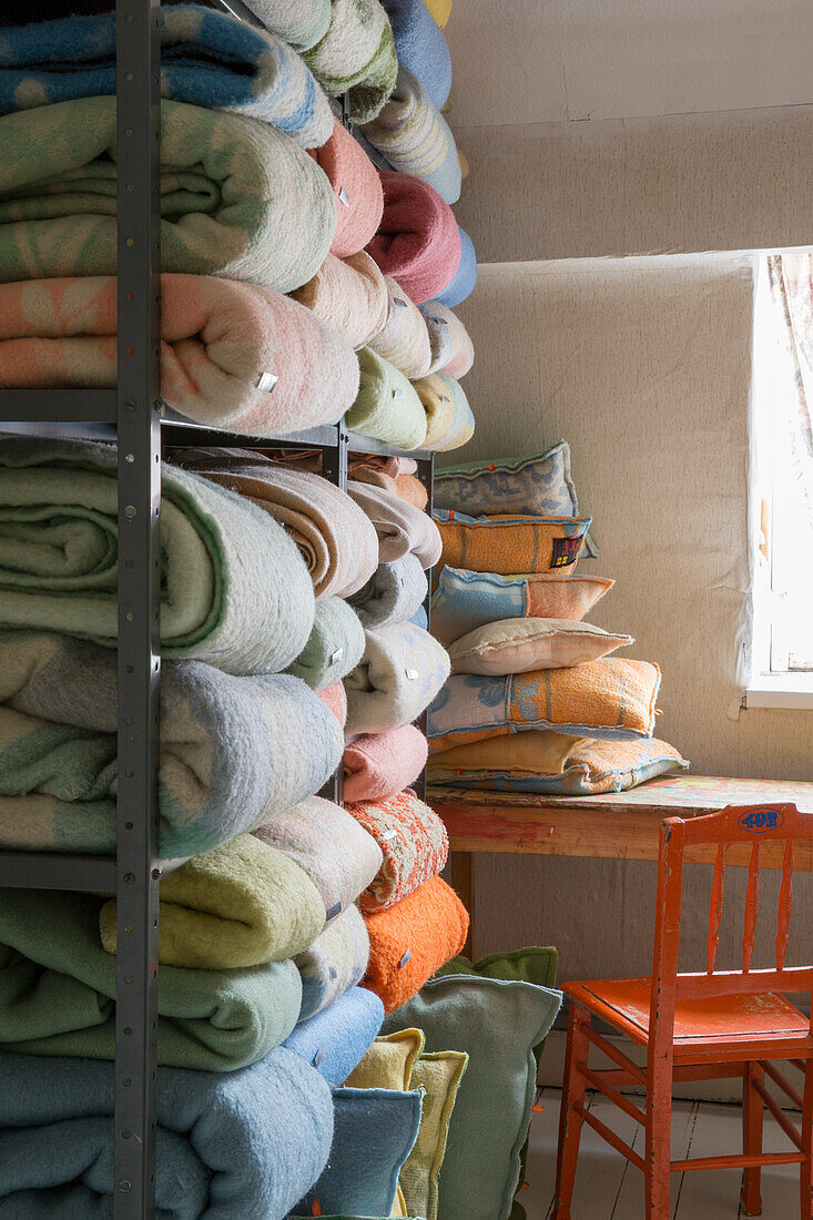 Shelf with folded blankets and cushions next to a desk with orange wooden chair