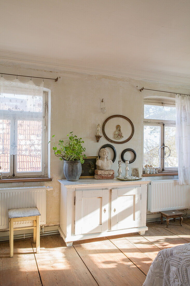 Vintage wooden chest of drawers, picture frame, bust and plant in bright living room