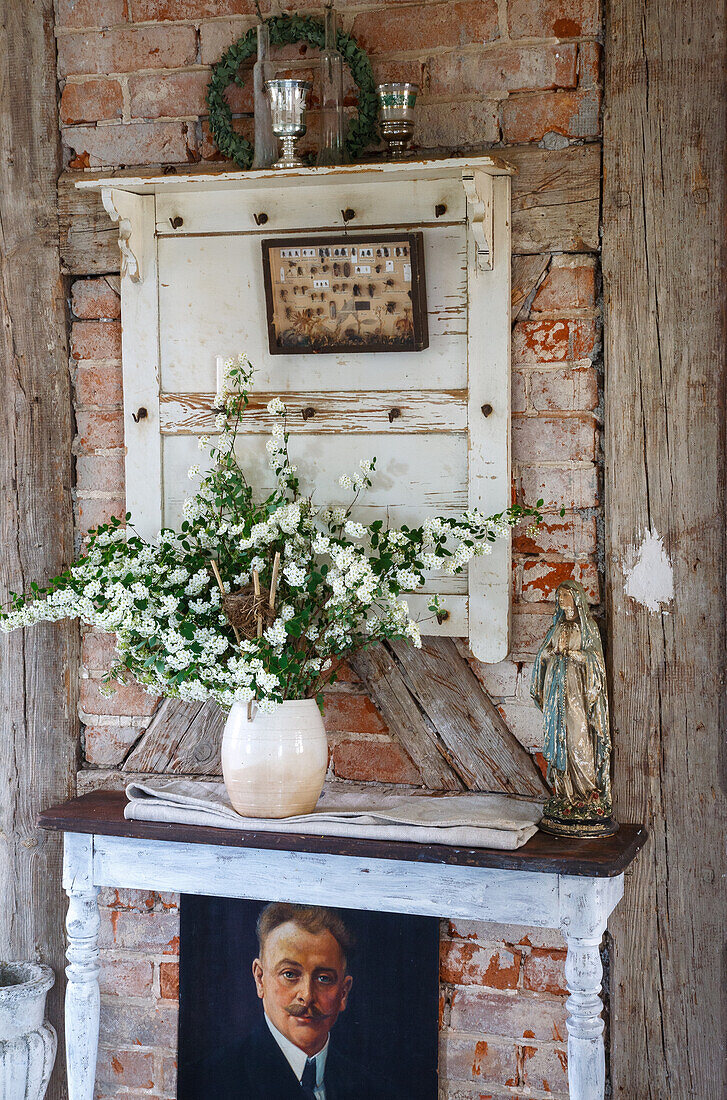 Vintage decoration in front of brick wall with bouquet of flowers and Madonna statue on rustic side table