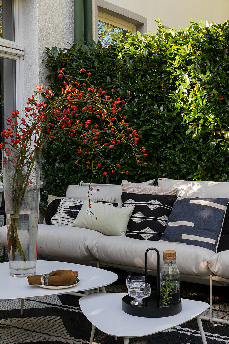 Modern styled patio with white sofa and patterned cushions in front of hedge