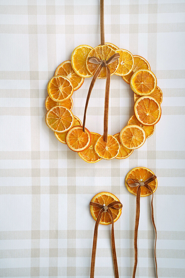 Decorative wreath and pendant made of dried orange slices against a chequered background