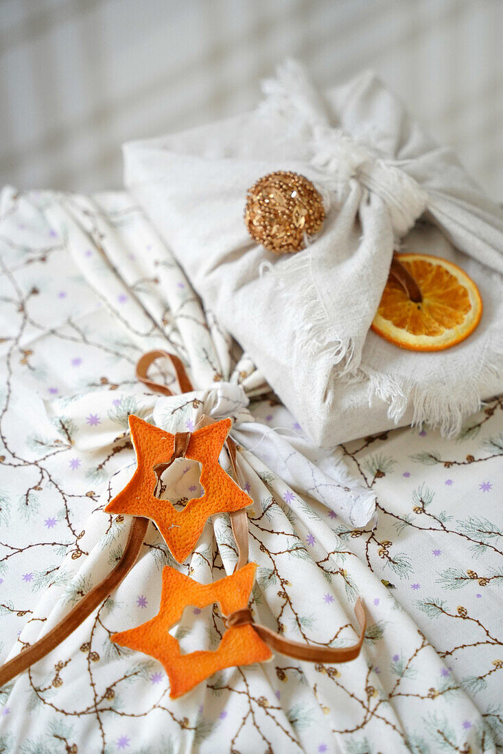 Weihnachtsgeschenke in Stoffverpackung mit getrockneten Orangenscheiben und Sternen aus Orangenschalen