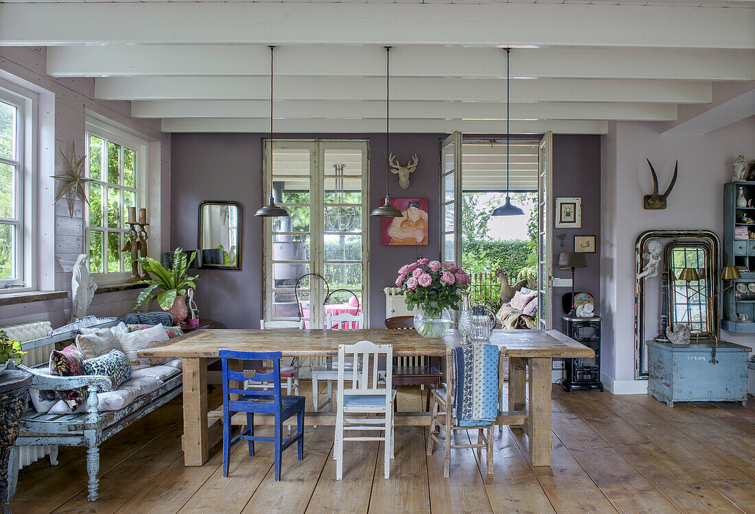 Holztisch und bunte Stühle in eklektischem Esszimmer mit großen Fenstern