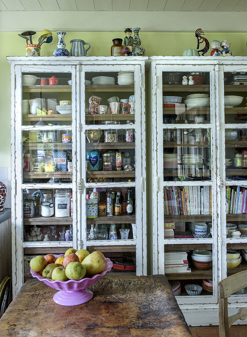 Vintage display cabinets with crockery and decor, fruit bowl on rustic wooden table