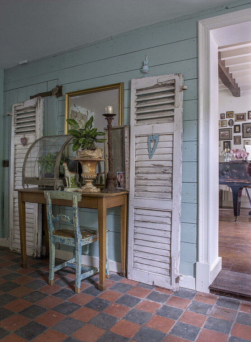 Vintage entrance area with desk, decorative plant arrangement and antique wood shutters