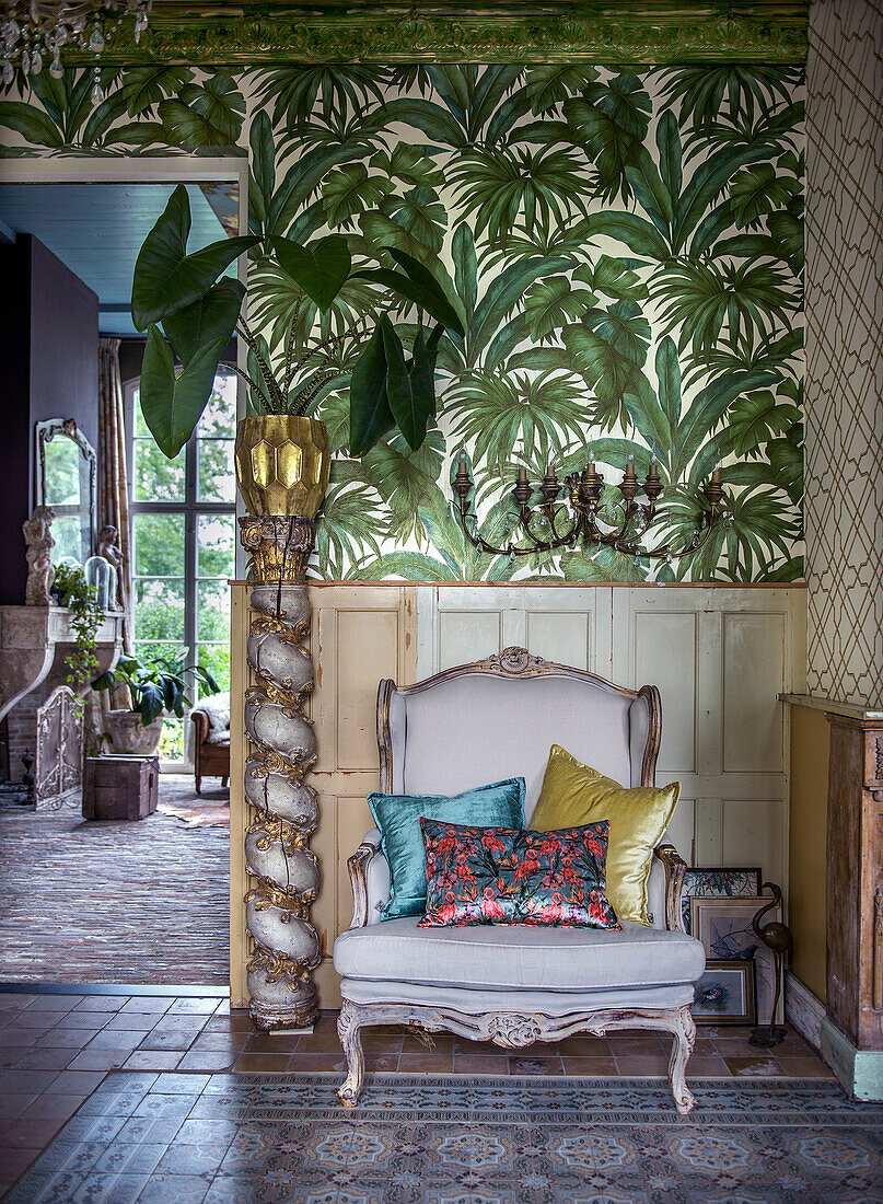 Baroque chair with colorful pillows in front of tropical wallpaper in living room corner