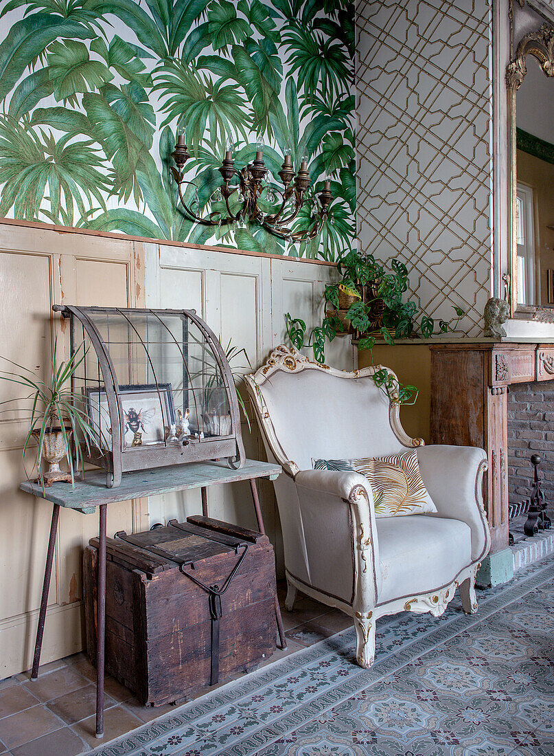 Vintage armchair next to rustic fireplace and jungle wallpaper in the living room