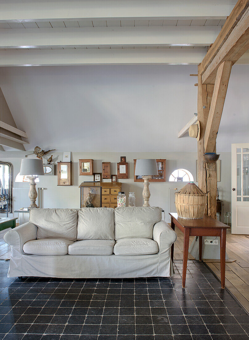 Sofa on black tiled floor in rustic living room with wooden beams