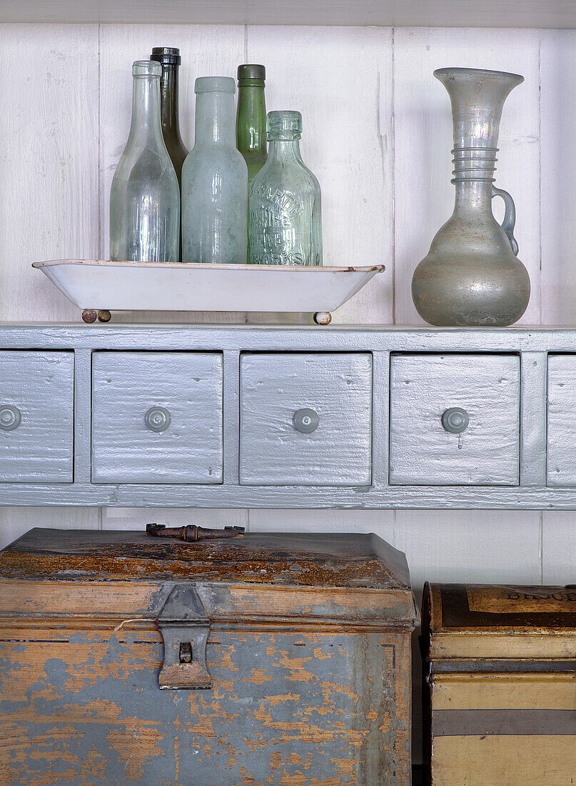 Display cabinet with antique glass bottles and jug above worn metal crates