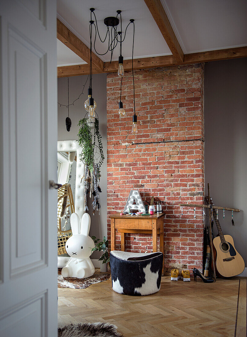 Raum mit Hasenlampe, Backsteinwand, Kuhfellhocker und Gitarre