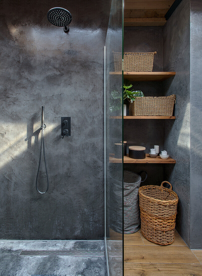 Moderne Dusche mit grauer Betonwand und geflochtene Körbe auf Holzregalen