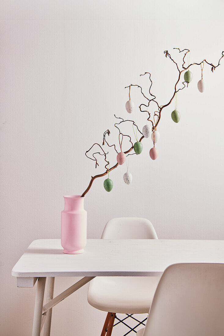 Zweig von Korkenzieherweide mit pastellfarbenen Ostereiern auf Tisch