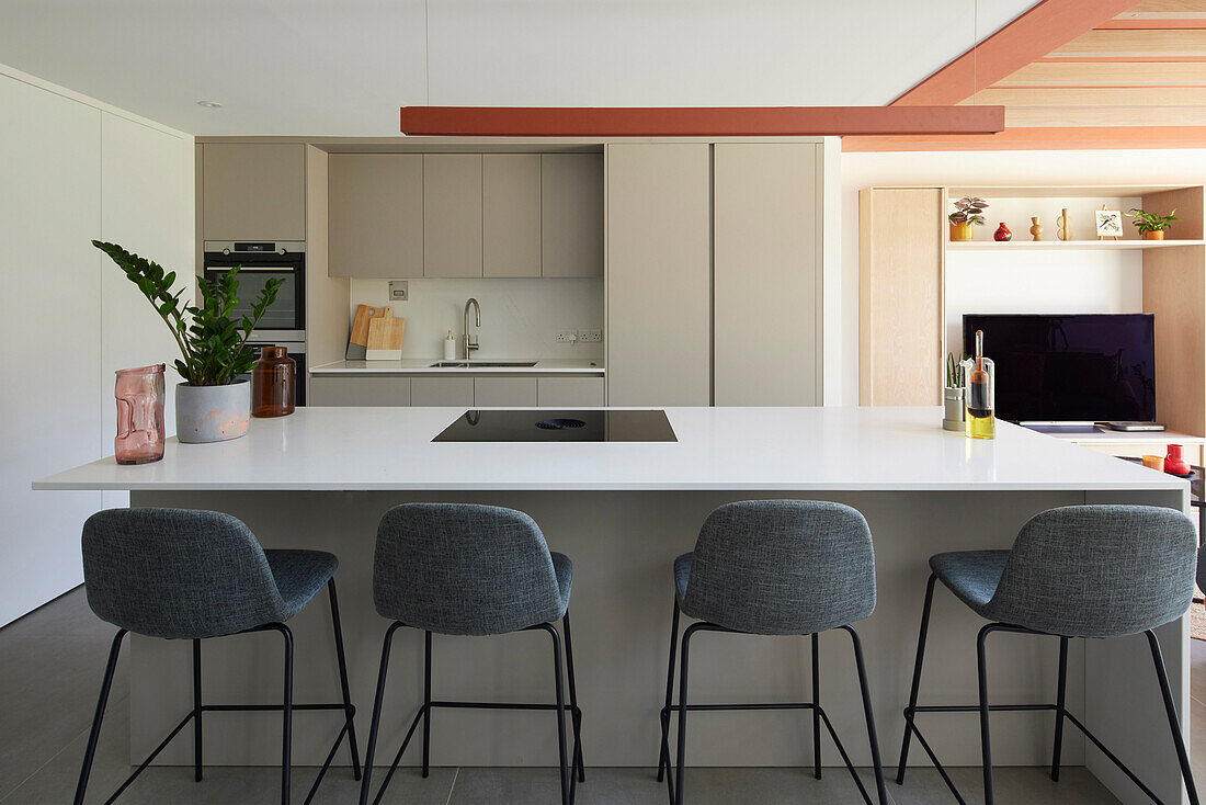 Moderne Küche mit weißer Arbeitsplatte, korallroten Akzenten und grauen Barhockern