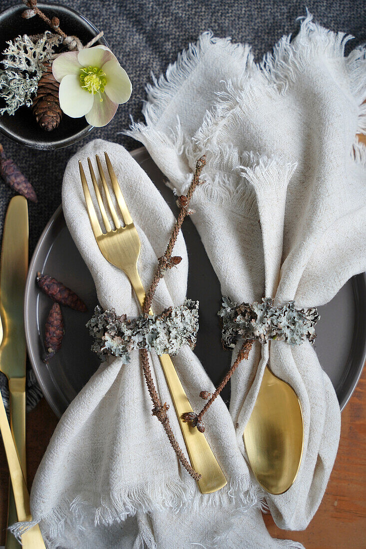 Festive table decoration with gold-colored cutlery and napkin rings made from natural materials