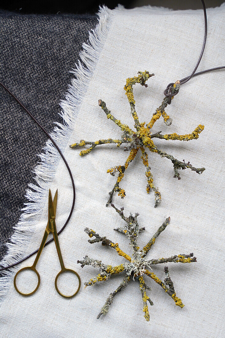 DIY-Sterne aus Zweigen und Flechten auf Textiluntergrund neben Schere