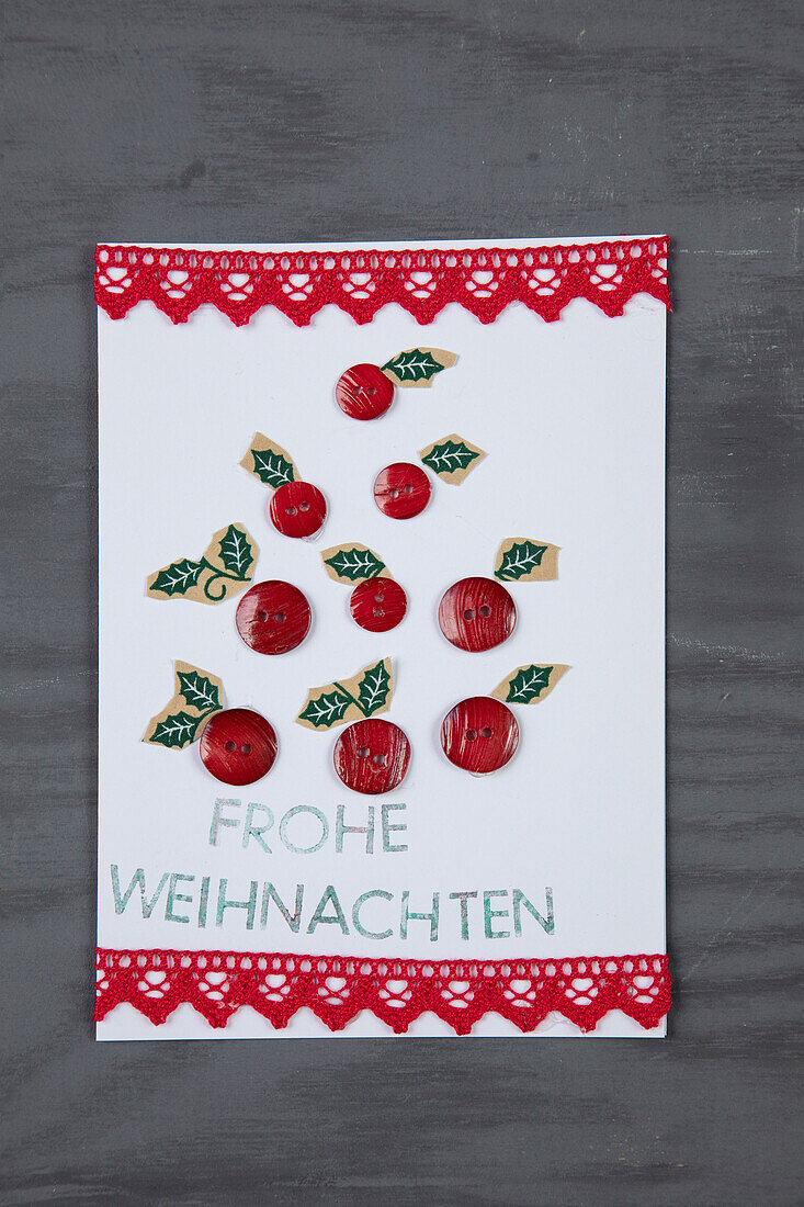 Handgefertigte Weihnachtskarte mit Knöpfen und Spitzenband auf grauem Holzuntergrund